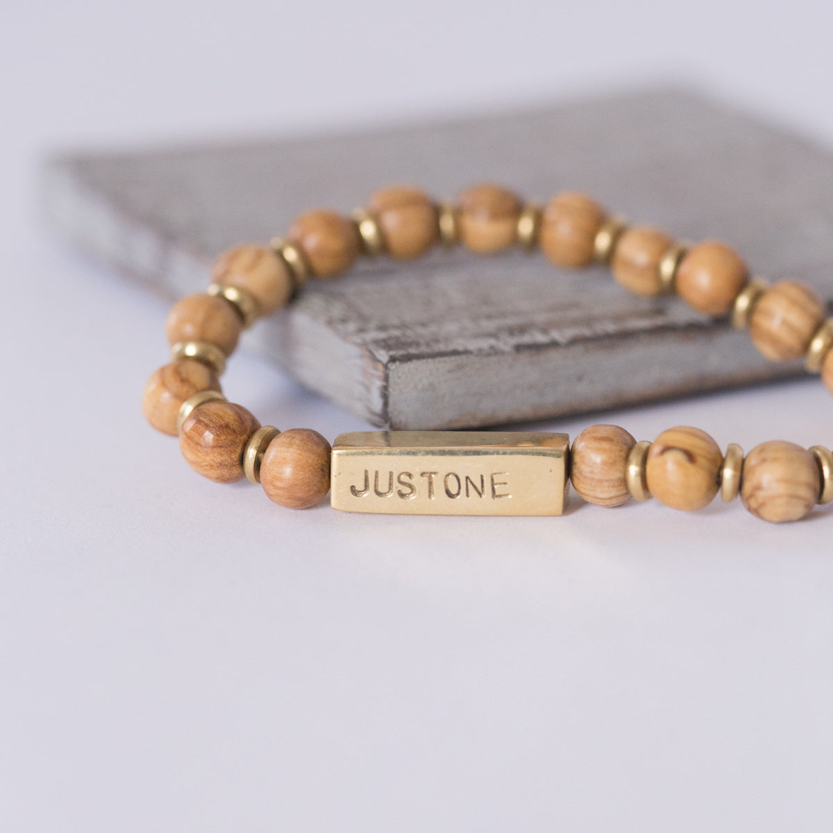 JustOne's stretch bracelet made with handcrafted wooden beads and brass bar that says JustOne, handcrafted in Kenya