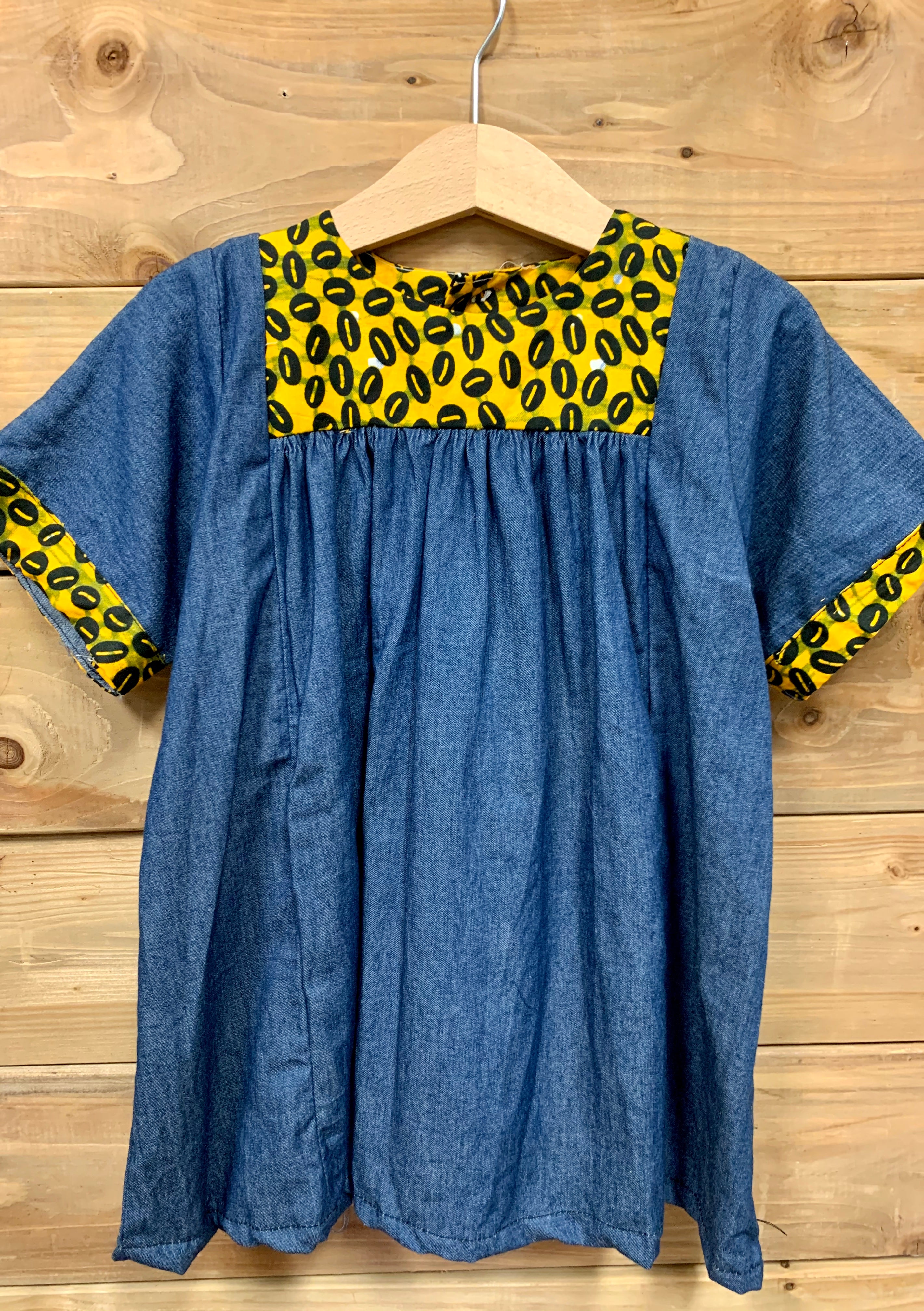 JustOne's small blue dress with design around the collar and cuffs of the sleeves, hand-sewn in Uganda