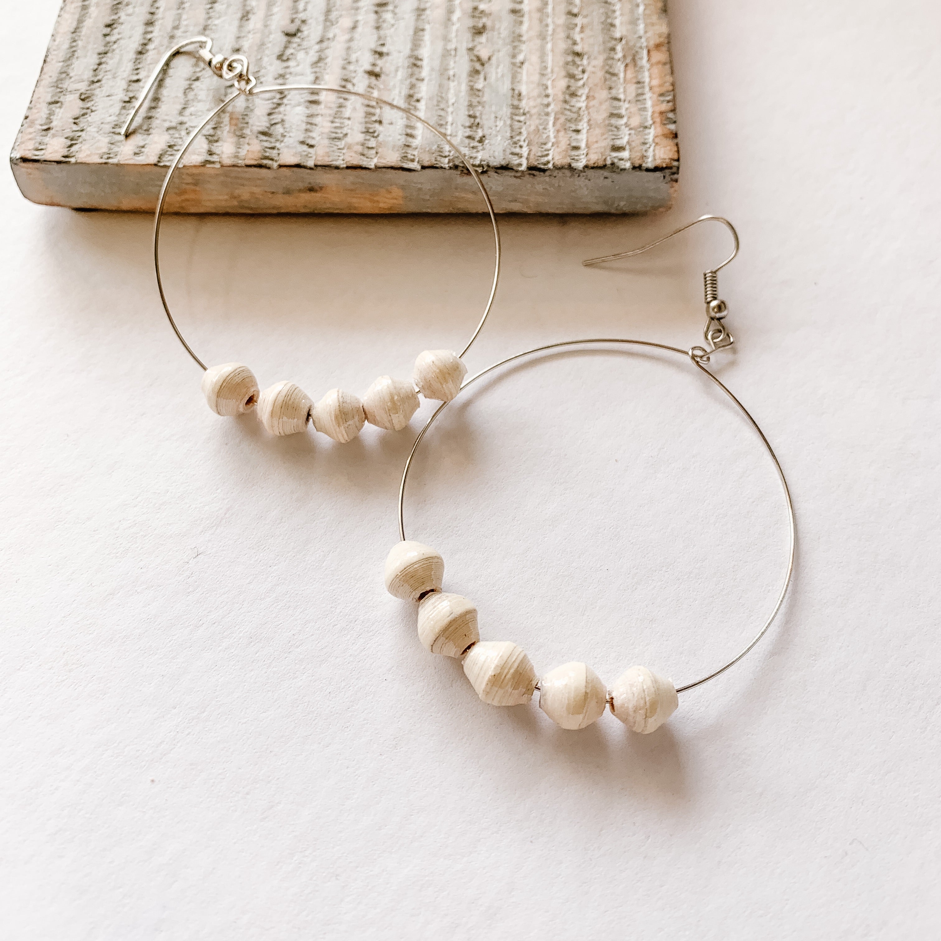JustOne's silver hoop earrings with five white paper beads on the bottom of the hoop, handcrafted in Uganda